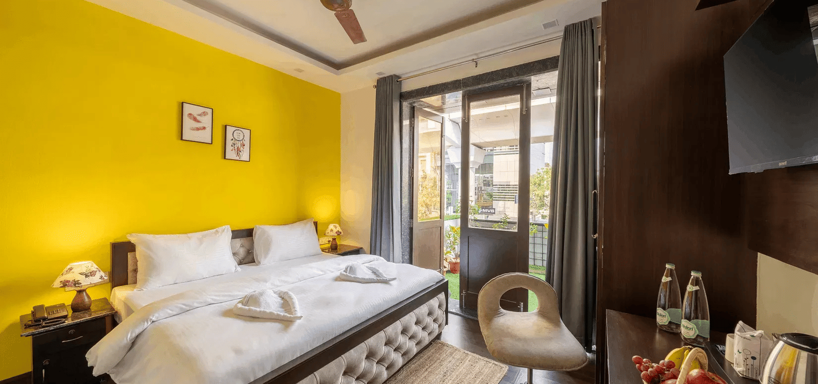 A brightly lit yellow-walled hotel room with a double bed and a large window - Lime Boutique Bed & Breakfast | Nehru Place Metro